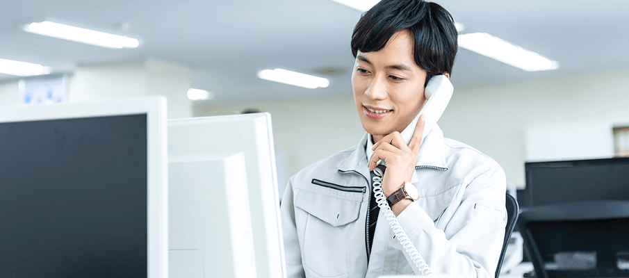 オフィスで電話対応をする明るい表情の作業着姿のスタッフ