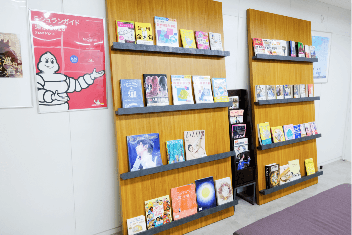 日販アイ・ピー・エス株式会社 様 オフィス内にある、書籍やポスターが展示されたマガジンラックとベンチの様子。